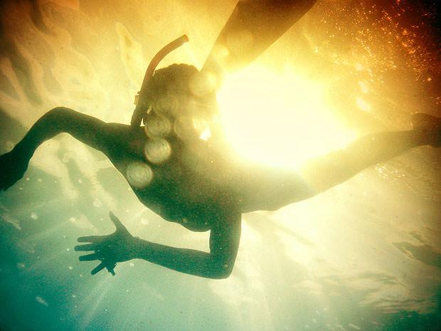 Boy swimming underwater with orange and blue light behind